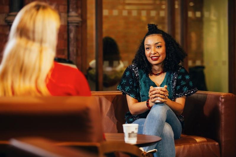 A woman sitting and enjoying a coffee with a colleague, engaged in a friendly conversation.