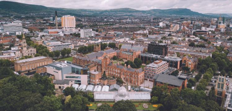 An aerial view of the main campus from above Botanic gardens showing the Lanyon and surrounding buildings and belfast skyline in the background