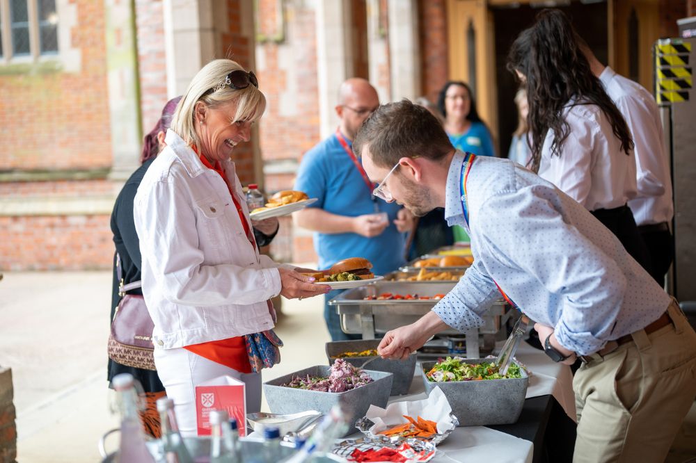 Staff lining up to choose their food at the Carers Week barbecue in Queen's quadrangle/cloisters, June 2023