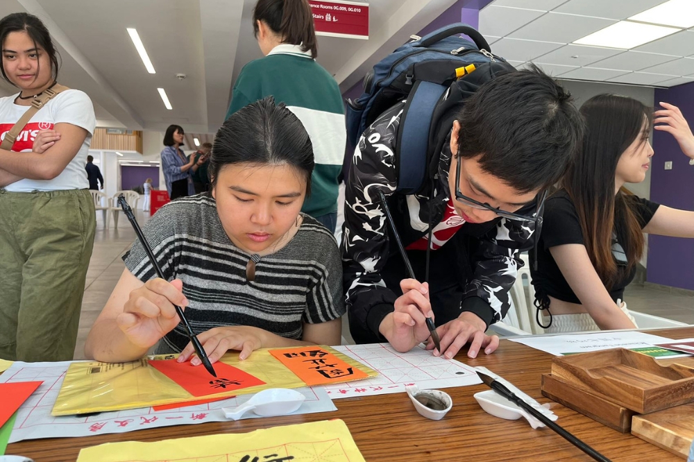 Students trying out Chinese calligraphy at the Language Centre stall table, Summer Social and Wellbeing event, Peter Froggatt Centre
