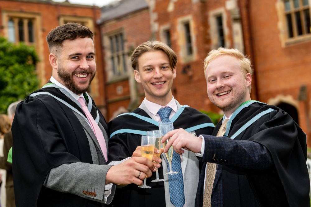 three male graduates smiling and clinking glasses