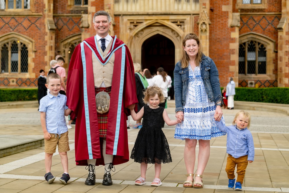 male graduate in traditional Scottish kilt and sporran celebrating with wife and children outside the Lanyon Building