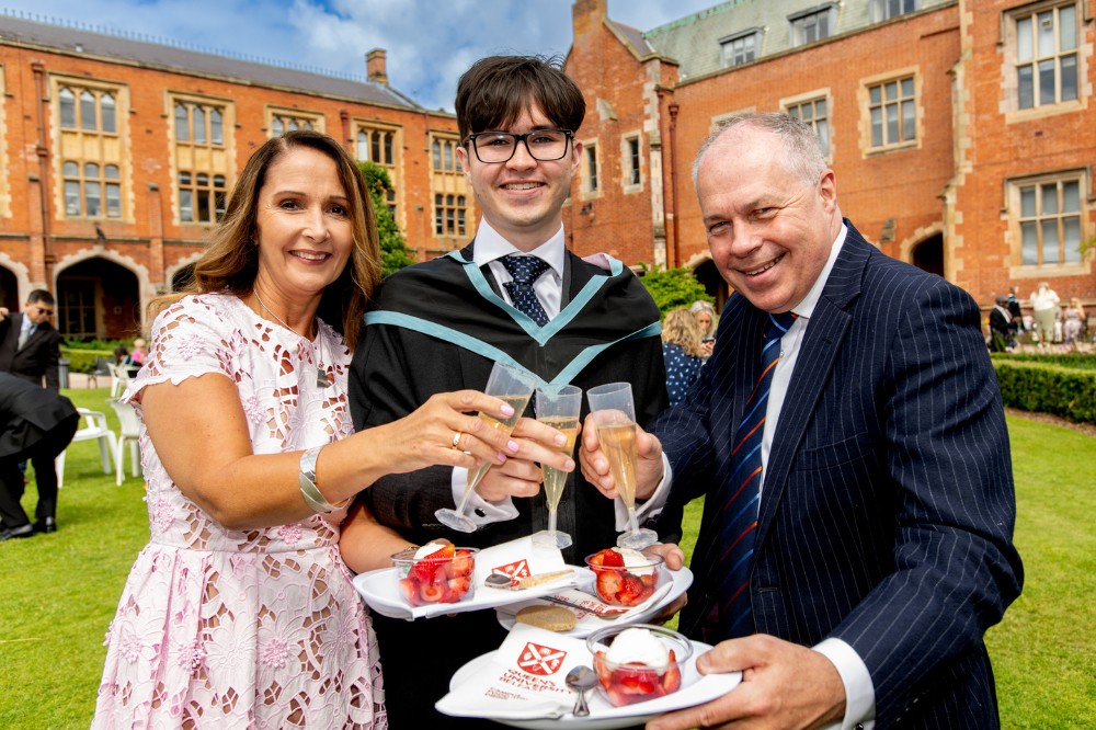 young male graduate celebrating with his parents, with strawberries and cream and sparkling refreshment