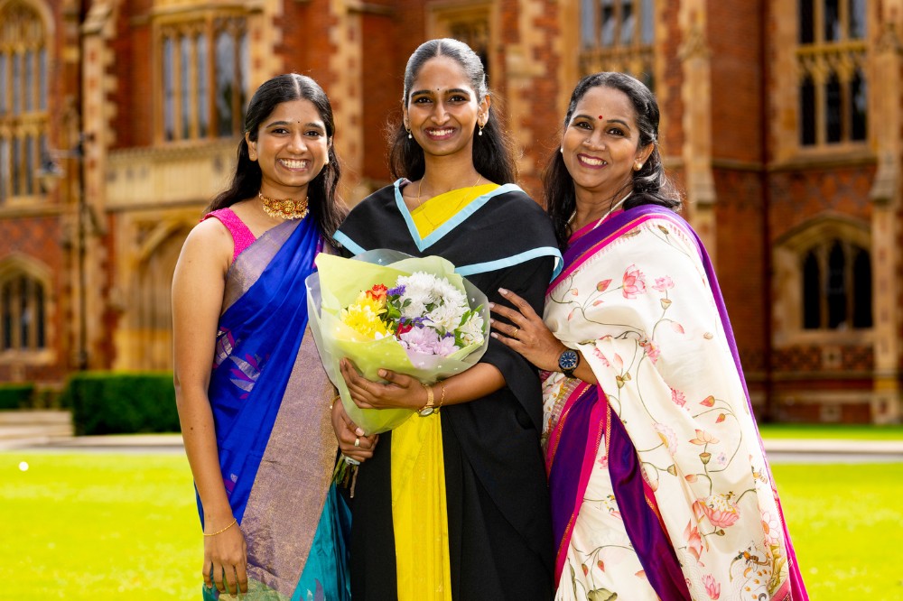 new International female graduate holding a bouquet of flowers and flanked by female friends on Queen's front lawn