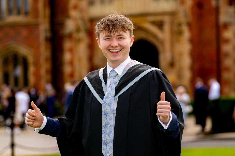 new male graduate smiling and giving the thumbs up outside Queen's Lanyon Building