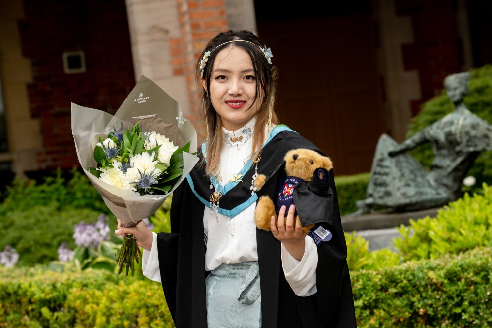 new Chinese female graduate holding bouquet of flowers and graduation teddy bear