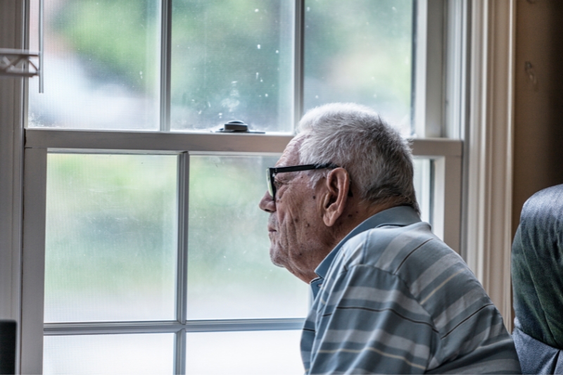seated elderly man wearing glasses looking out of a window