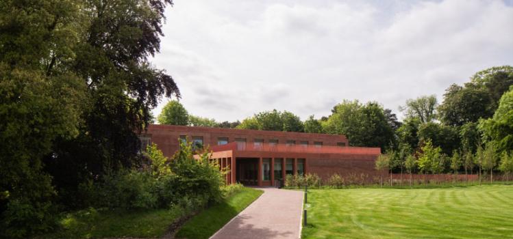 Image of Queen's business School, a red brick building set in a green landscape with trees