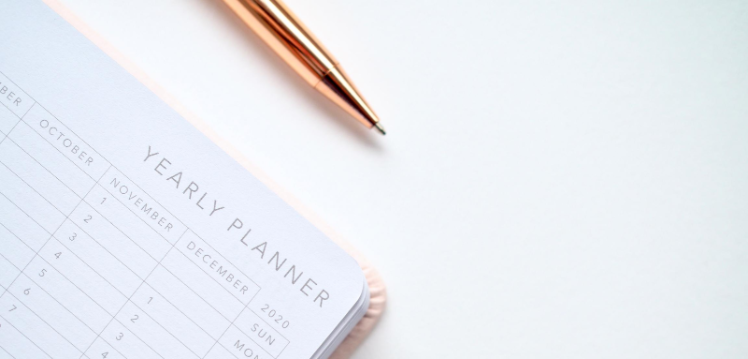 corner of an open calendar or yearly planner with a gold coloured biro pen sitting at the top