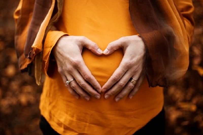 pregnant woman in dark yellow top holding her hands over her bump in a heart shape