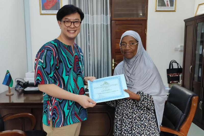 man of Asian origin and woman of African origin posing for the camera while holding a certificate in an office space with photographs on the background wall