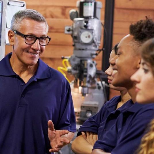 male technician showing/explaining a piece of technical equipment to three young trainees/students/workers