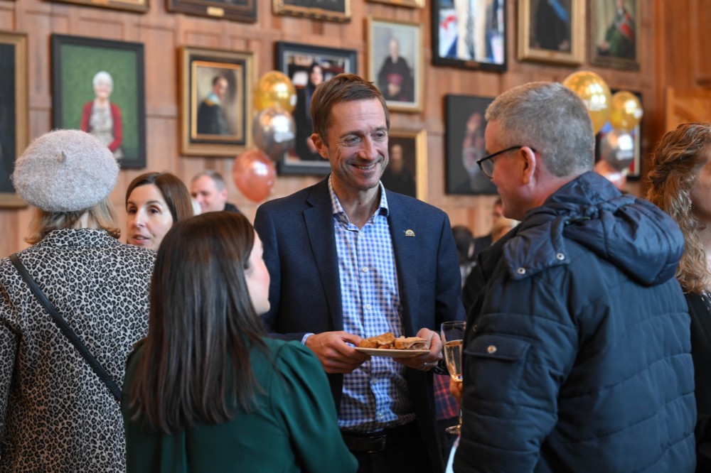 people chatting and mingling at an event in an old wood-paneled hall with portraits hanging on the wall in the background
