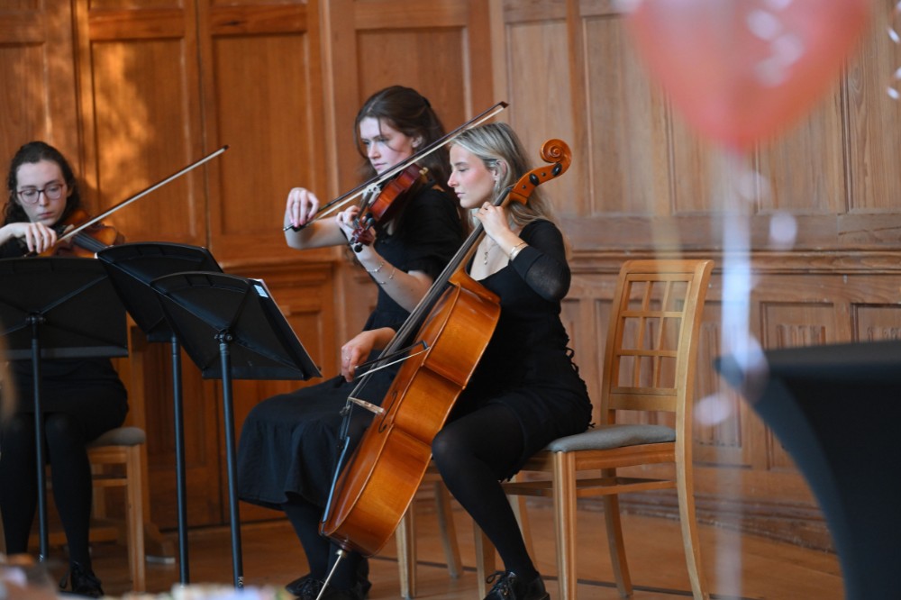 three female members of a string quartet playing at a formal event in an old wood-paneled hall