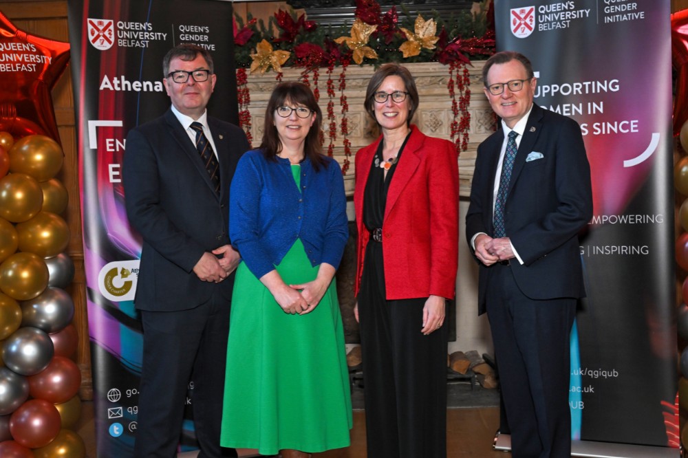 two men and two women posing for a photo in an old wood-paneled event hall with pop-up stands and presentation screen in the background