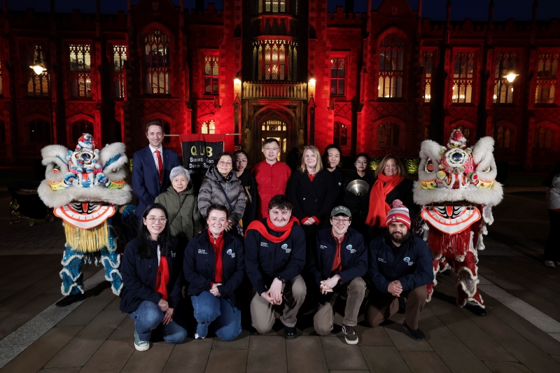 group of people framed by Chinese dragon dancers standing outside the red-illuminated Queen's University Belfast Lanyon Building, 29 January 2025