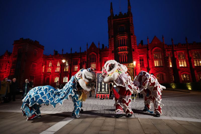 traditional Chinese Lion Dance being performed in front of an old building illuminated red against a dark blue evening sky