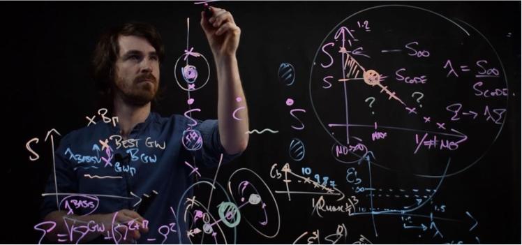 Physicist writing equations and diagrams on a board, illuminated with colourful markings. The board features mathematical symbols, graphs, and complex calculations, with the scientist focused intently on their work.