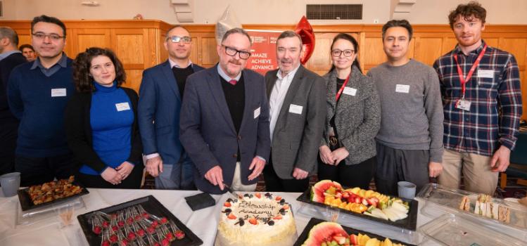 Professor Archie Clements, pictured in the Canada Room with Fellows and members of staff, cuts a cake that's inscribed 'Fellowship Academy 4 Years'