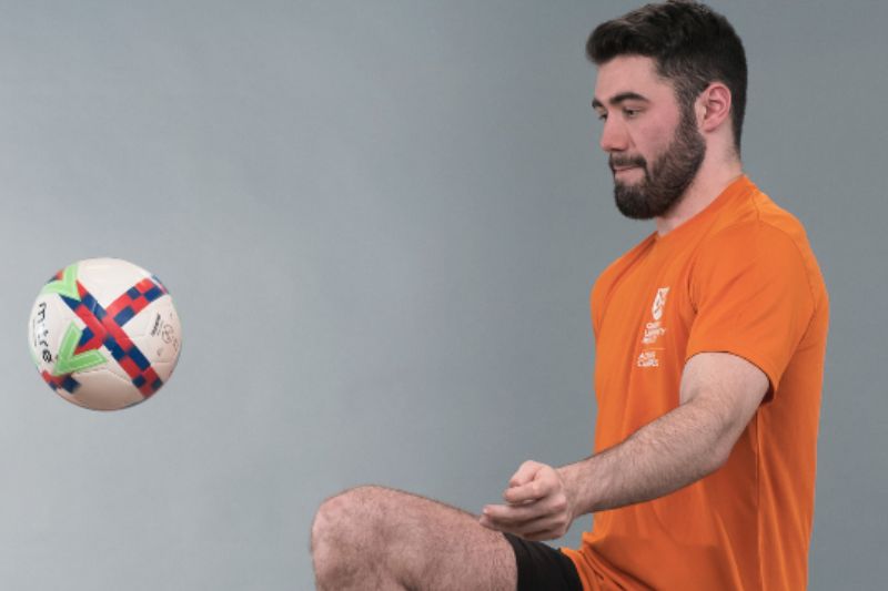 man in orange t-shirt playing 'keepy uppies' with a football