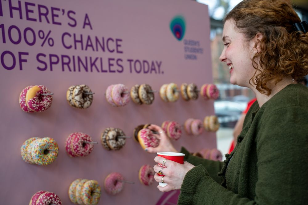 Student selecting a doughnut from a display board during a campus wellbeing event.