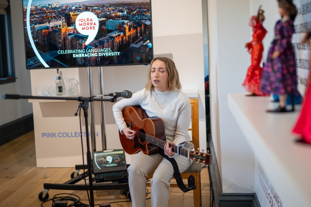 young woman playing acoustic guitar and singing at the launch of Queen's new Staff Network for Promoting Linguistic Diversity and Minority Languages, in the Naughton Gallery