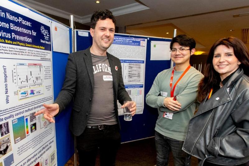 postdoc researcher discussing his research poster with two others at an indoor showcase event