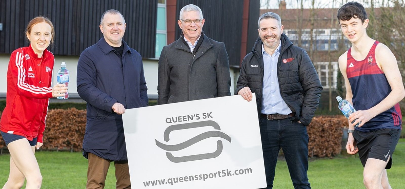 sporting students and staff members holding Queen's Sport 5k run plaque outside the Physical Education Centre, Queen's University Belfast