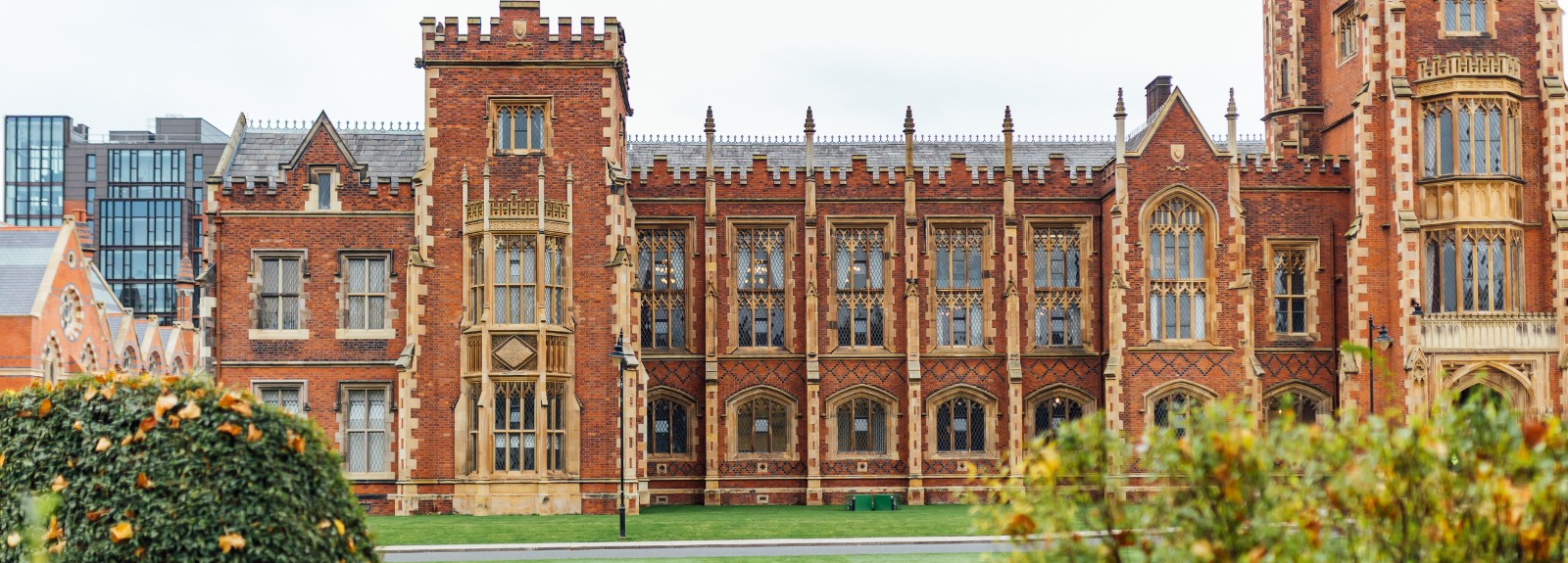 Victorian redbrick building façade, and modern tower block detail in top left, pictured with bushes and greenery in the foreground
