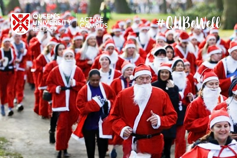 large group of people jogging while dressed in Santa costumes. Image includes Queen's University Belfast Active Campus logo and #QUBeWell campaign brand device.