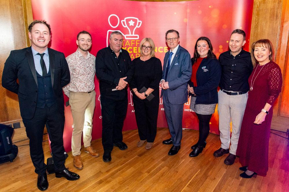 group of five men and three women smiling for the camera in front of a large pop-up stand at an indoor event