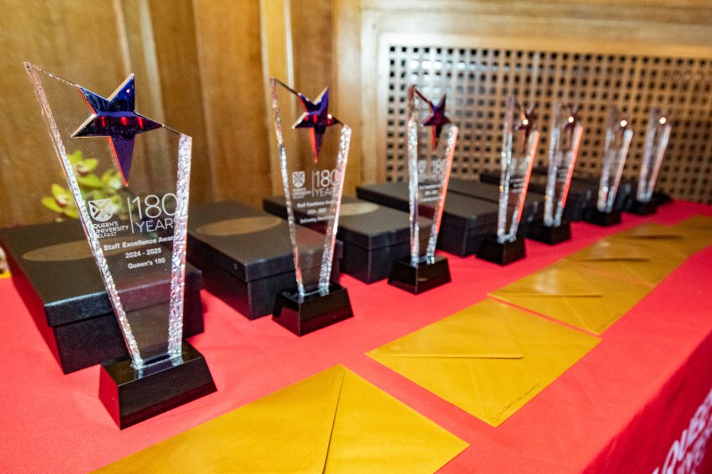 Seven crystal trophies sitting on a table at and awards event. Wording on the trophies reads' Queen's University Belfast 180 Years / Staff Excellence Awards 2024-25'.