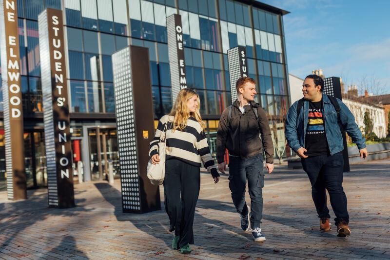 Three students walking past the front of One Elmwood building
