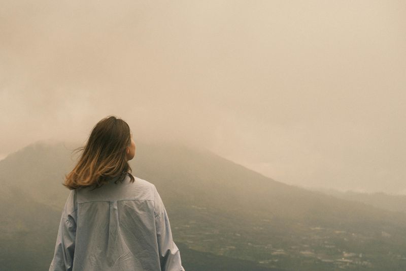lone woman with her back turned to the camera looking into a foggy landscape background including a mountain